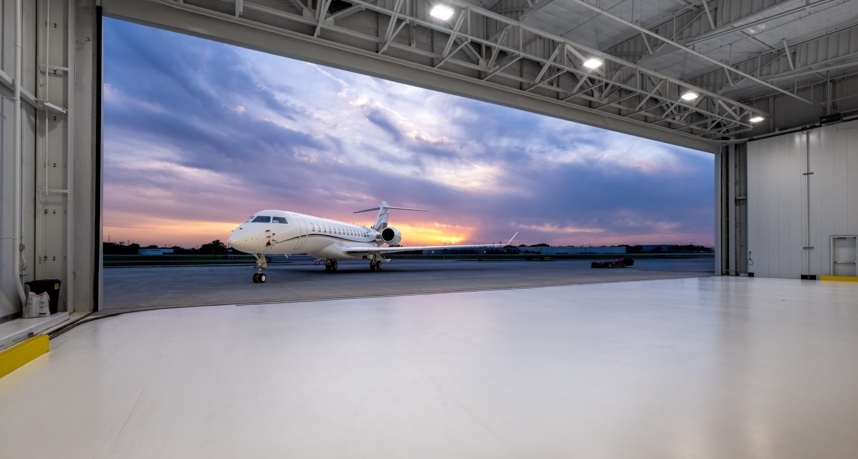Bombardier Challenger business jet on the ramp at dusk, viewed from inside an open aircraft hangar