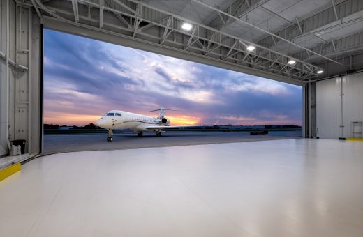 Bombardier Challenger business jet on the ramp at dusk, viewed from inside an open aircraft hangar